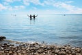 Two girls silhouettes in the water, gravel beach and blue sky with clouds