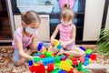 Two girls sisters in medical masks sit at home and play in a children`s colorful constructor during isolation Royalty Free Stock Photo