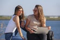 Two girls sit on a bench in the summer park. They look at the laptop screen Royalty Free Stock Photo