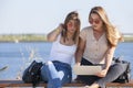 Two girls sit on a bench in the summer park. They look at the laptop screen Royalty Free Stock Photo