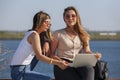 Two girls sit on a bench in the summer park. They look at the laptop screen Royalty Free Stock Photo