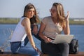 Two girls sit on a bench in the summer park. They look at the laptop screen Royalty Free Stock Photo