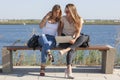 Two girls sit on a bench in the summer park. They look at the laptop screen Royalty Free Stock Photo