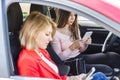 Two girls sit in car in front seats with phones Royalty Free Stock Photo