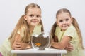 Two girls sit at a round aquarium with goldfish and look in the frame Royalty Free Stock Photo