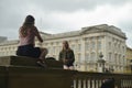 Two girls sitting on the fence in front of Buckingham palace