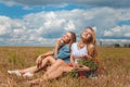 Two girls sitting on meadow with wildflowers and