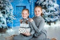 two girls are sitting near the Christmas tree. red-haired sisters unfold gifts near the fireplace. the interior is blue Royalty Free Stock Photo