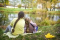 Two girls are sitting on the shore of the lake under the willows in the autumn park