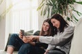 Two girls sitting at sofa, watching something funny at tablet, smiling, laughing