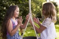 Two Girls Sitting On Swing Playing Clapping Game