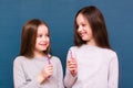 Two girls are smiling, looking at each other and holding toothbrushes in their hands on a blue background. Royalty Free Stock Photo