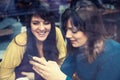 Two girls smiling and using smart phone in a cafe Royalty Free Stock Photo