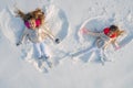 Two Girls on a snow angel shows. Smiling children lying on snow with copy space. Funny kids making snow angel. Top view. Royalty Free Stock Photo