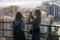 Two girls stand on a hill and look at the beautiful panorama of the Spanish city of Malaga on a warm