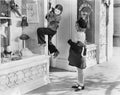 Two girls on the street with one climbing on a display window