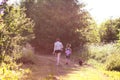 Two girls in summer dresses walking with small black dog on footpath in the green summer field near the lake Royalty Free Stock Photo