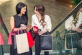 Two girls talk about shopping using smartphone on escalator in the mall and hold the bags in hands Royalty Free Stock Photo