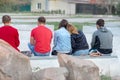 Two girls and three guys are sitting on a bench in a park on the waterfront, one girl laid her head on the shoulder of the other