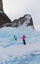 Two girls-tourists travel in winter on the ice of frozen Baikal Lake near the icy cliffs