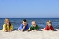 Two girls and two boys in colorful t-shirts lying on sandy beach Royalty Free Stock Photo