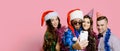 Two girls and two guys 20-25s in holiday hats and santa claus caps and tinsel shoot a video or take a selfie for social networks