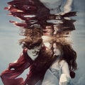 Two girls underwater in a blue and red dress