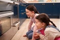 Two Girls Waiting For Cupcakes To Bake Looking Into Oven In Kitchen At Home Together