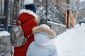 Two girls walking along the winter snowy street of the city, children are holding hands, back view Royalty Free Stock Photo