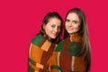 Two girls, in a warm blanket, posing on red with side space. Winter concept Royalty Free Stock Photo