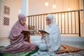 two girls wearing Muslim clothes with hijab reciting the Quran