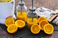 Two glass bottles on the table with orange juice and straw, electric squeezer and oranges cut in half Royalty Free Stock Photo