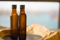 Two glass brown transparent faceted bottles empty and full with vegetable oil with green caps stands on a black plate on paper. Royalty Free Stock Photo