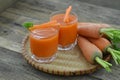 Two glass of carrot juice and tasty ripe carrot on wicker basket on wooden table