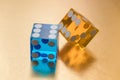 Two glass dice, blue and yellow, on a gold background in sunlight. Result six and unknown.