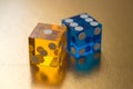 Two glass dice, yellow and blue, on a gold background in sunlight. Result one and six. Royalty Free Stock Photo