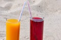 Two glass glasses with juice of mango and cherry with tubules. Sandy beach on a summer day Royalty Free Stock Photo