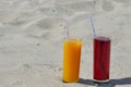 Two glass glasses with juice of mango and cherry with tubules. Sandy beach on a summer day Royalty Free Stock Photo