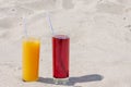 Two glass glasses with juice of mango and cherry with tubules. Sandy beach on a summer day Royalty Free Stock Photo