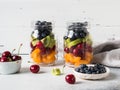 Two glass jars with berries and fruits. Fruit salad with apricots, kiwi, cherries and blueberries in glass jars on white Royalty Free Stock Photo