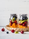 Two glass jars with berries and fruits. Fruit salad with apricots, kiwi, cherries and blueberries in glass jars on white Royalty Free Stock Photo