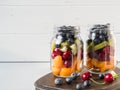 Two glass jars with berries and fruits. Fruit salad with apricots, kiwi, cherries and blueberries in glass jars on white Royalty Free Stock Photo