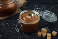 Two glass jars of homemade caramel with crystals of salt on black wooden table Royalty Free Stock Photo