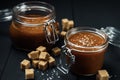 Two glass jars with homemade salted caramel and pieces of brown sugar with salt crystals Royalty Free Stock Photo