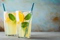 Two glass with lemonade or mojito cocktail with lemon and mint, cold refreshing drink or beverage with ice on rustic blue Royalty Free Stock Photo