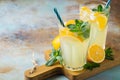 Two glass with lemonade or mojito cocktail with lemon and mint, cold refreshing drink or beverage with ice on rustic blue Royalty Free Stock Photo