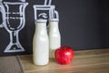 Two glass white bottles and a fresh apple on the table.