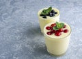 Two glass of yellow mango or banana yogurt or smoothie on gray background. Turmeric Lassie lassi served with berries. Healthy