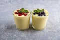 Two glass of yellow mango or banana yogurt or smoothie on gray background. Turmeric Lassie lassi served with berries. Healthy