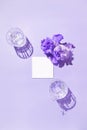 Two glasse with water and card note with iris flower on pastel lilac background. Summer refreshment concept. Sunlit flat lay. Royalty Free Stock Photo